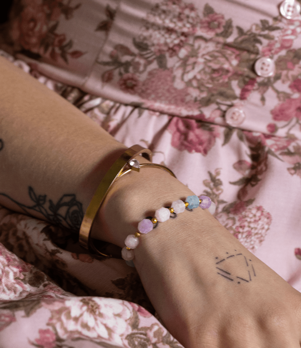 True Spring aquamarine and rose quartz bracelet layered with gold bangles over a floral dress