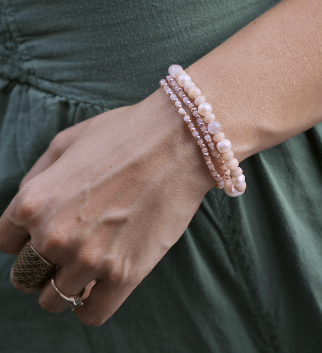 Blossom pink opal and pearl strands wrapped around a wrist beside a green dress