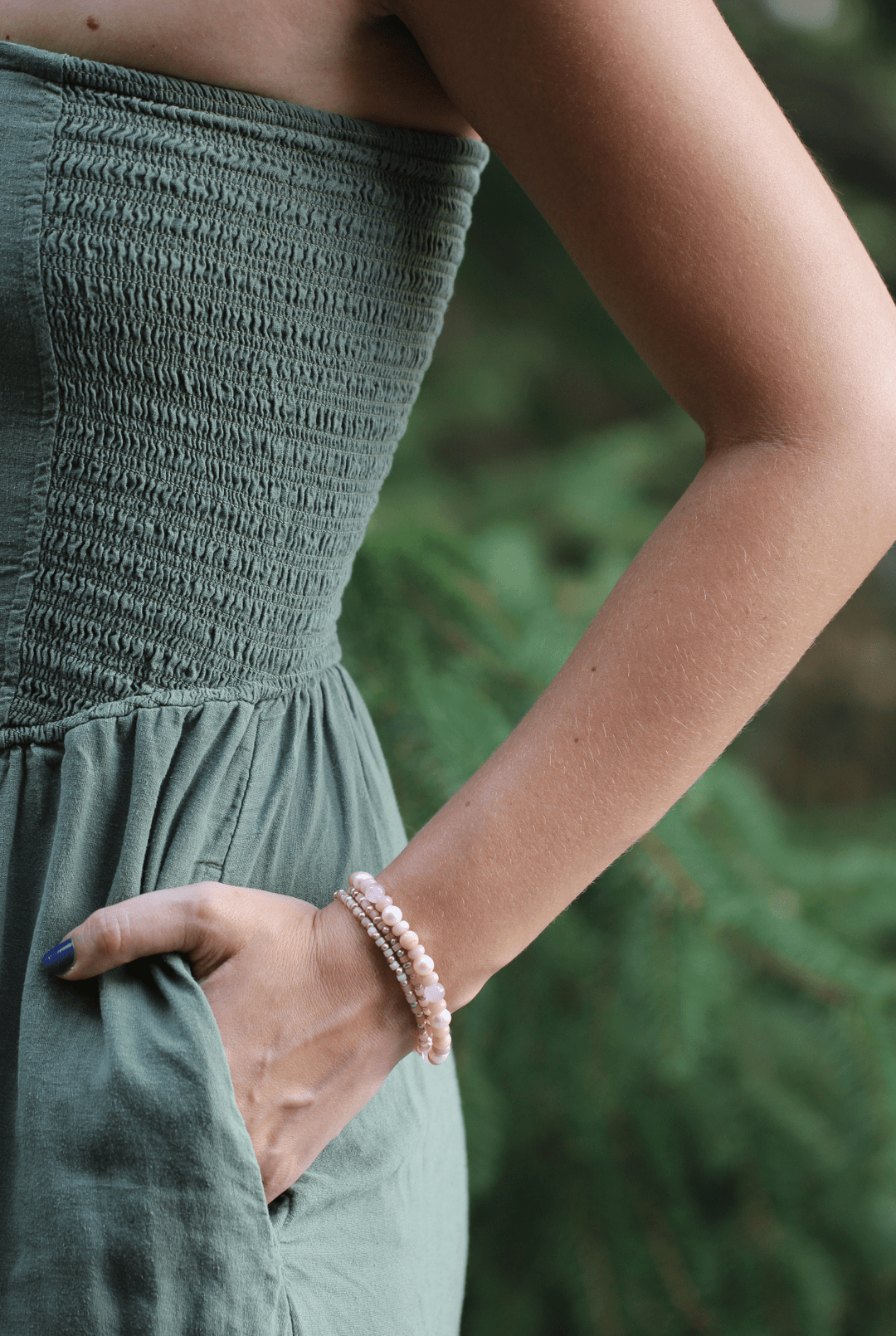 Blossom pink opal and pearl strands worn around a wrist with hand in a green dress pocket