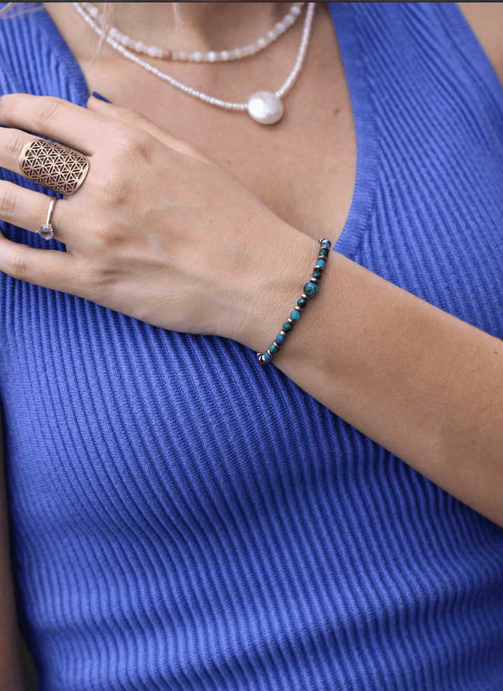 Earthrise bracelet worn on a bent wrist beside layered necklaces and a blue top