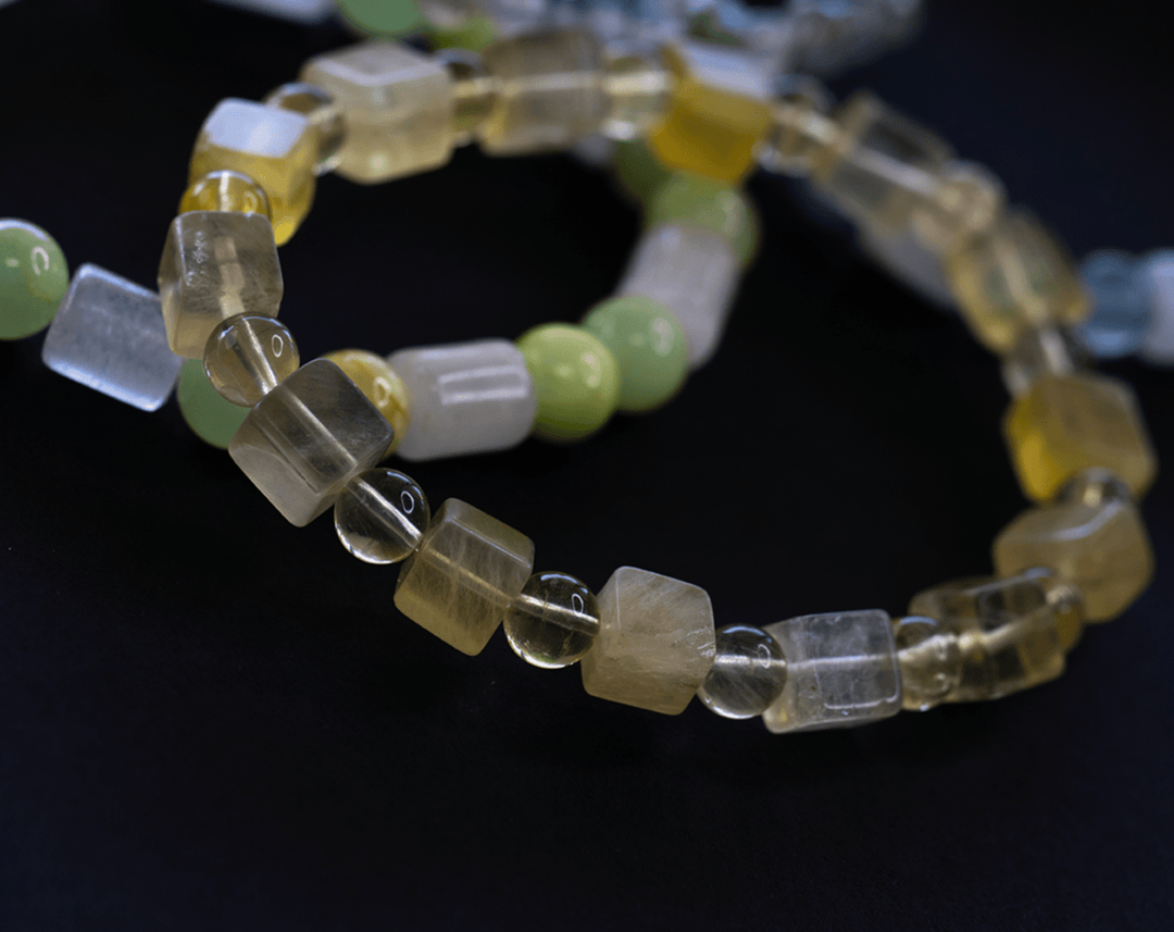 Golden yellow fluorite bracelet beside a pale green beaded bracelet on a dark surface
