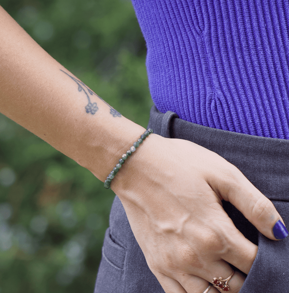 Green kyanite bracelet worn alone on a wrist with hand near a pocket and purple top