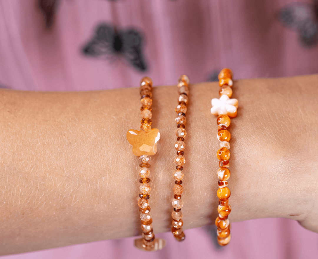 Monarch butterfly and Zuni daisy bracelets in an orange gemstone stack on a wrist
