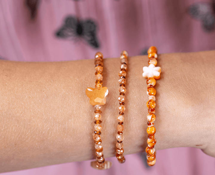 Monarch butterfly and Zuni daisy bracelets in an orange gemstone stack on a wrist