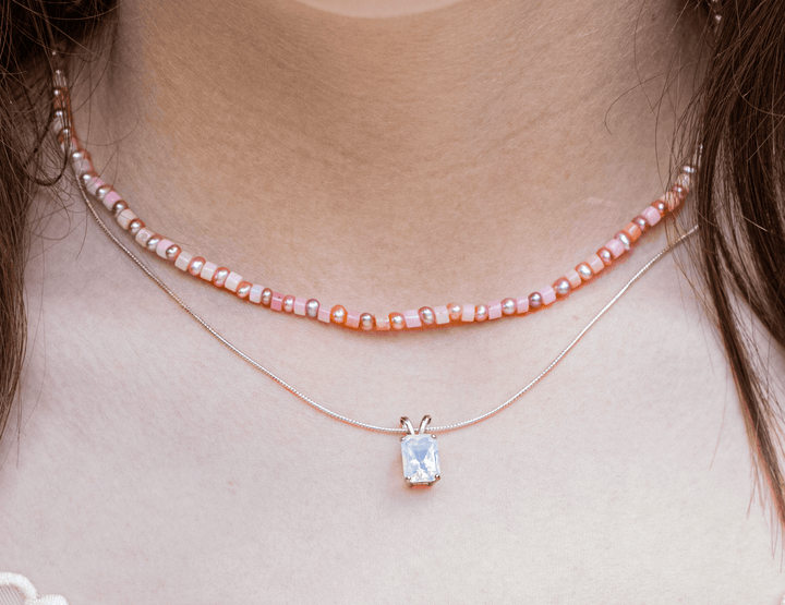 Rectangular Oregon opal pendant layered below a pink beaded necklace on a model
