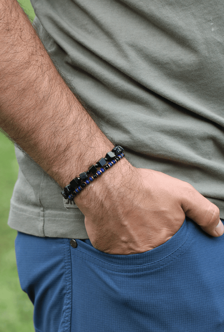 The Suit lapis and black tourmaline bracelet on a model’s wrist with one hand in a shorts pocket