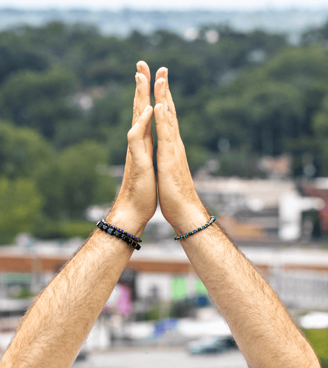 Two models wearing The Suit and a green gemstone bracelet with their hands pressed together outdoors