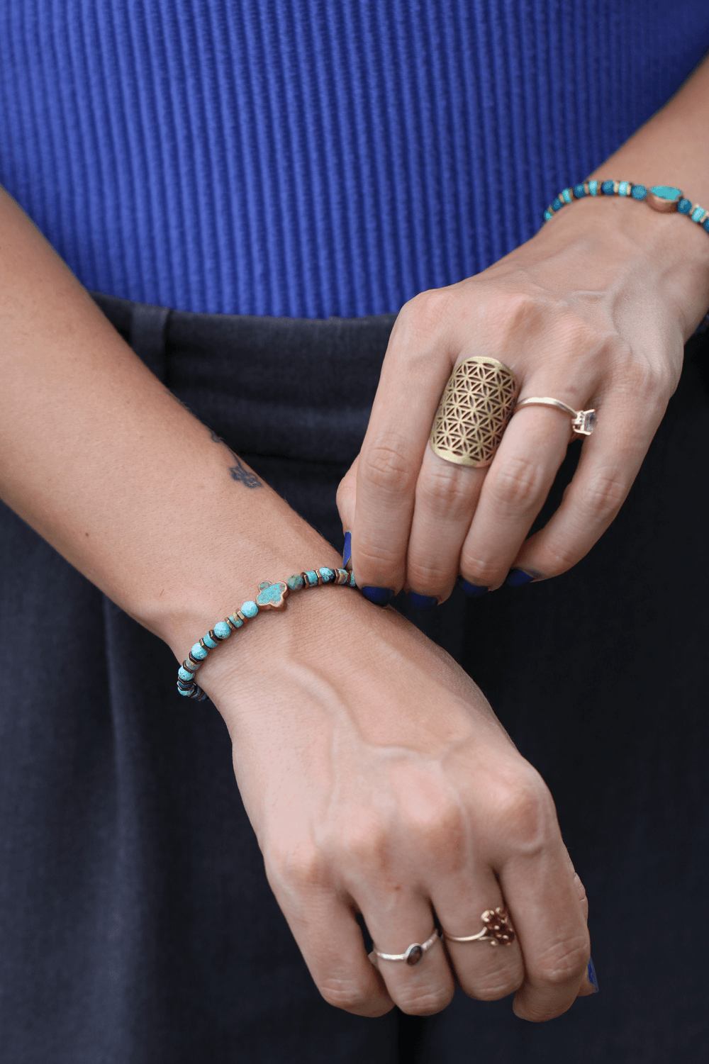 Patina Clove turquoise bracelet on a model's wrist with hands crossed near a blue top