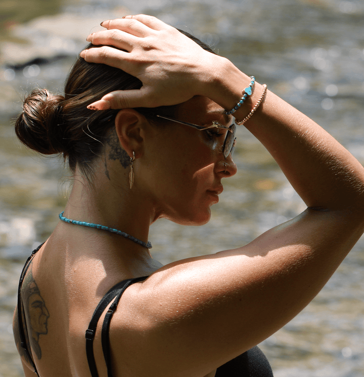 Patina Heart bracelet worn with a turquoise beaded necklace by a model beside the water