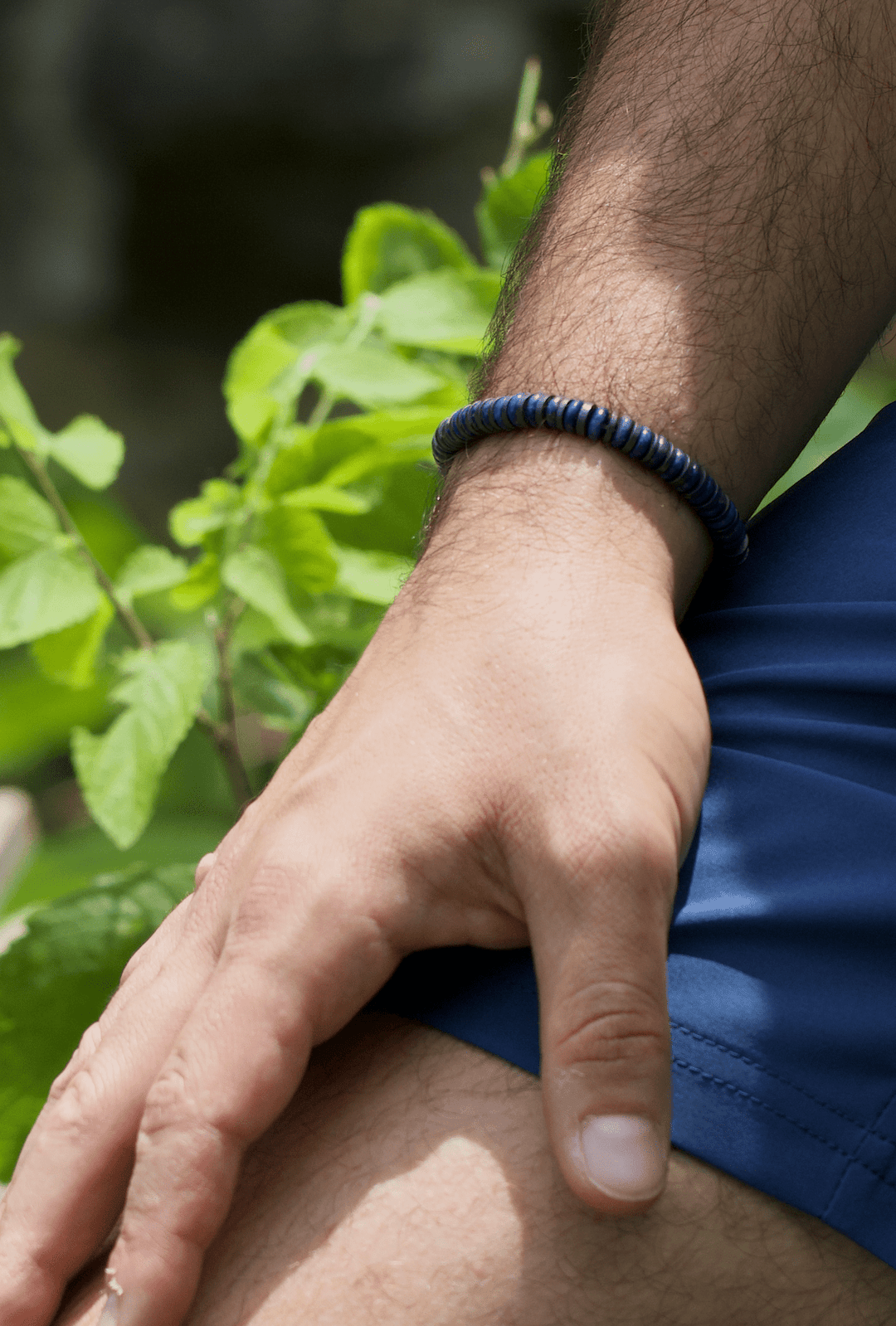 Royal Graphite blue lapis and titanium hematite bracelet on a wrist resting on a knee outdoors