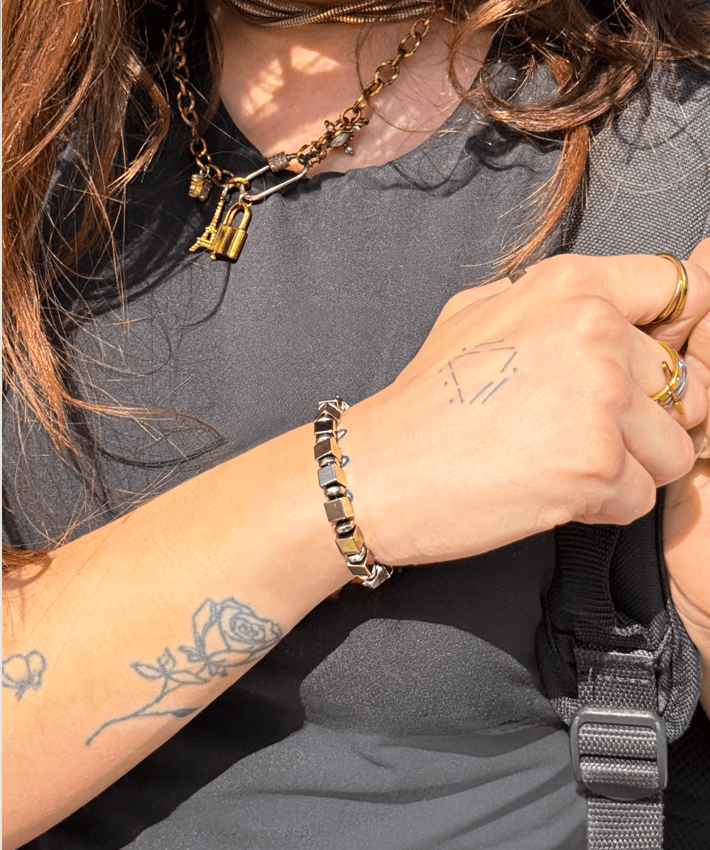 Sheen gold titanium pyrite bracelet on a tattooed wrist beside a black top outdoors