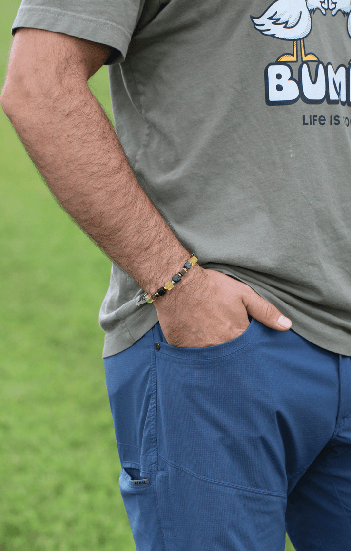 Model wearing the Shep black tourmaline and yellow fluorite bracelet with one hand in a shorts pocket