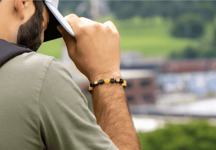 Shep black tourmaline and yellow fluorite bracelet on a raised wrist while adjusting a cap