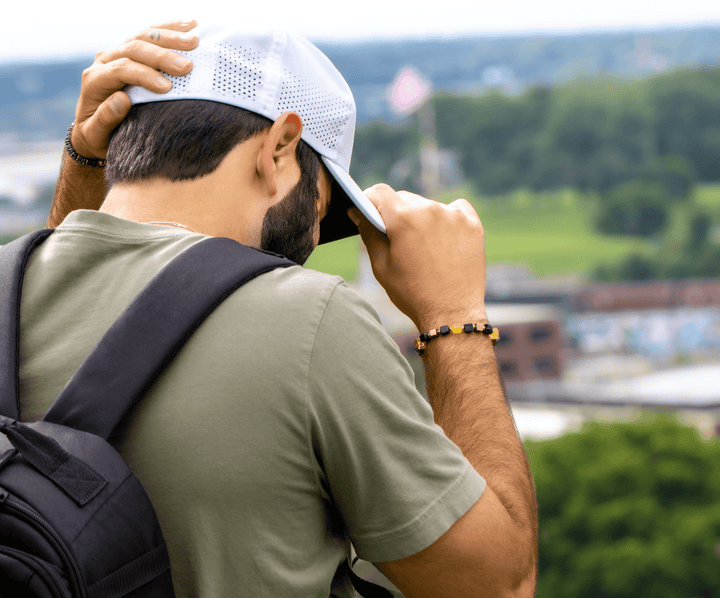 Model wearing the Shep black tourmaline and yellow fluorite bracelet while adjusting a cap outdoors