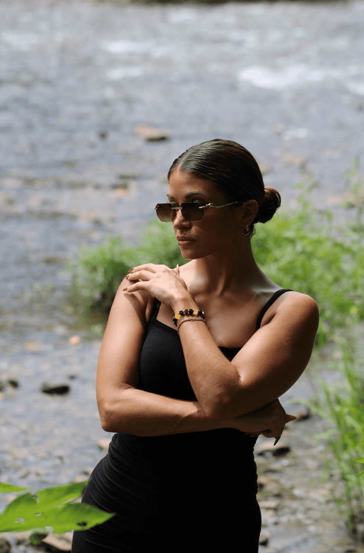 Model wearing the Shep black tourmaline and yellow fluorite bracelet beside a stream