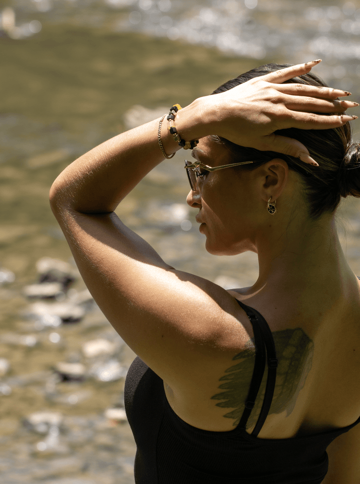 Model wearing the Shep black tourmaline and yellow fluorite bracelet with one arm raised by a stream
