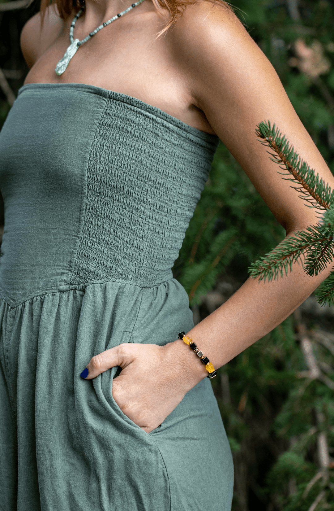 Model wearing the Shep black tourmaline and yellow fluorite bracelet beside greenery