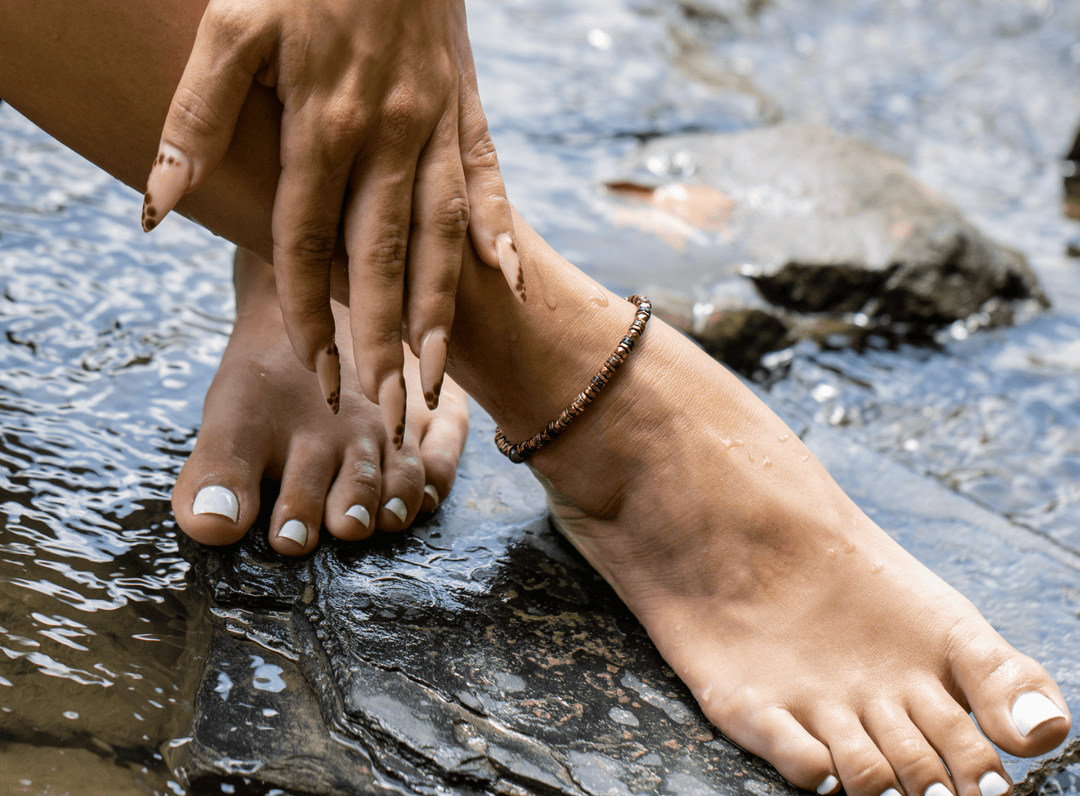 Tawny bronze biotite mica and titanium hematite anklet on a bare ankle above flowing water