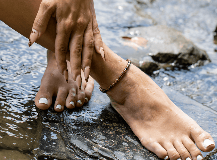 Tawny bronze biotite mica and titanium hematite anklet on a bare ankle above flowing water