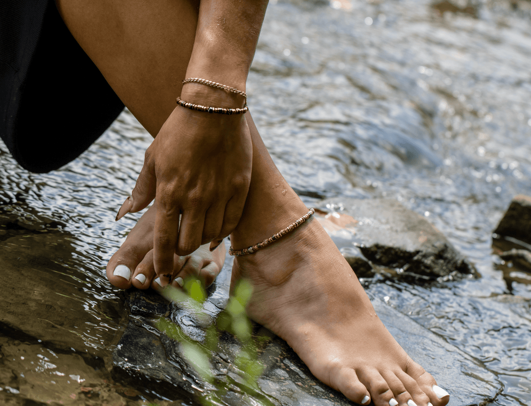 Model wearing the Tawny bronze biotite mica and titanium hematite stretch anklet beside a stream