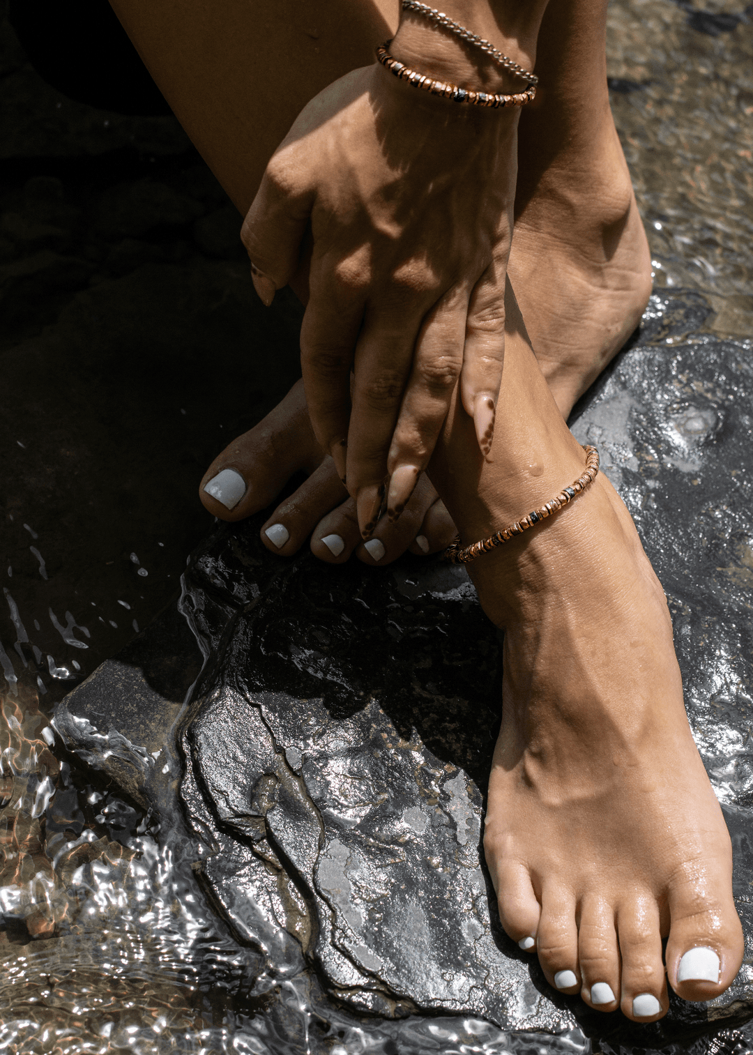 Tawny bronze biotite mica and titanium hematite anklet on a bare ankle beside a stream