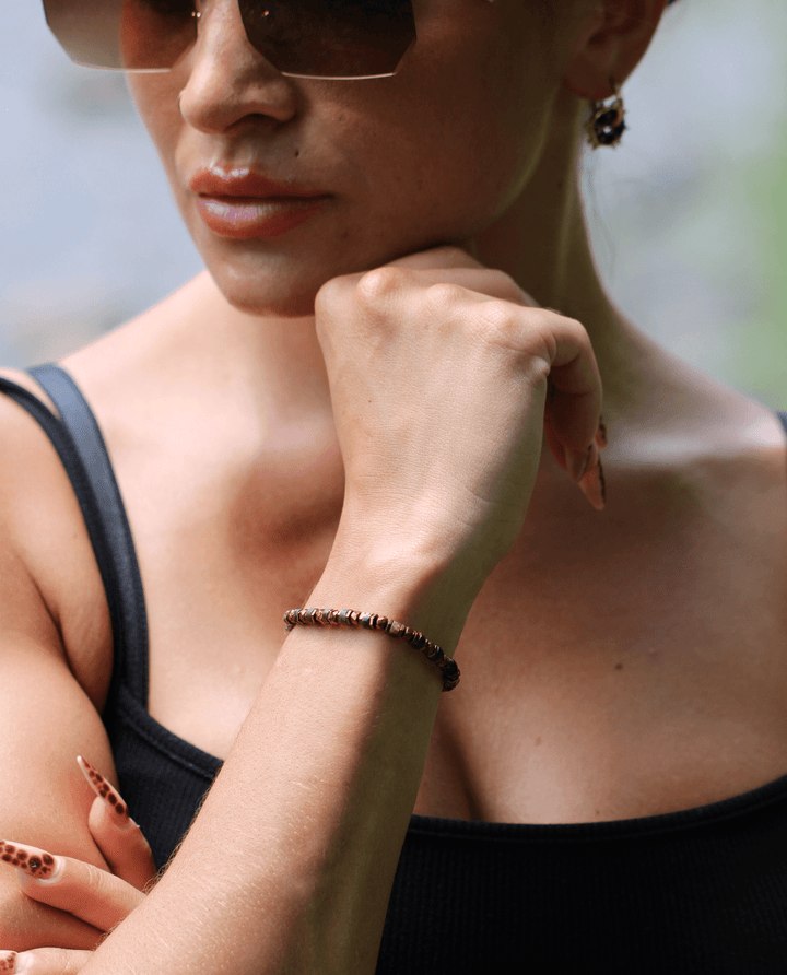 Tawny bronze biotite mica and titanium hematite bracelet on a model’s wrist with chin resting on hand