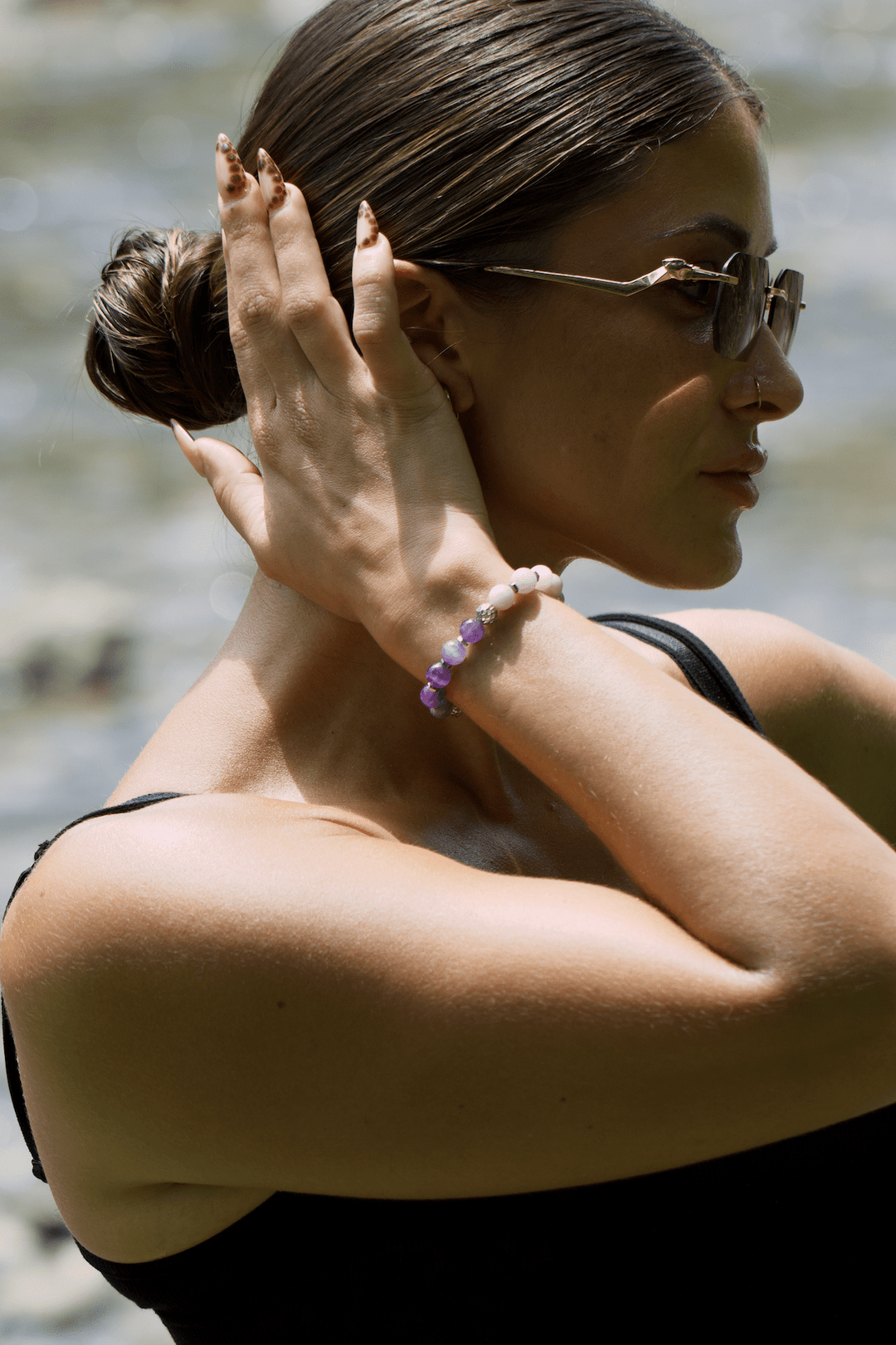Side view of a model wearing the Teach kunzite and amethyst bracelet with one hand raised to her hair
