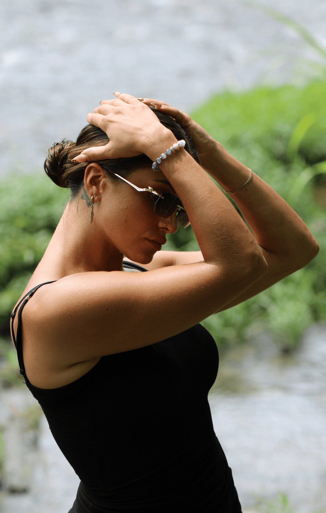Model wearing the Teach kunzite and amethyst bracelet with both arms raised beside a stream