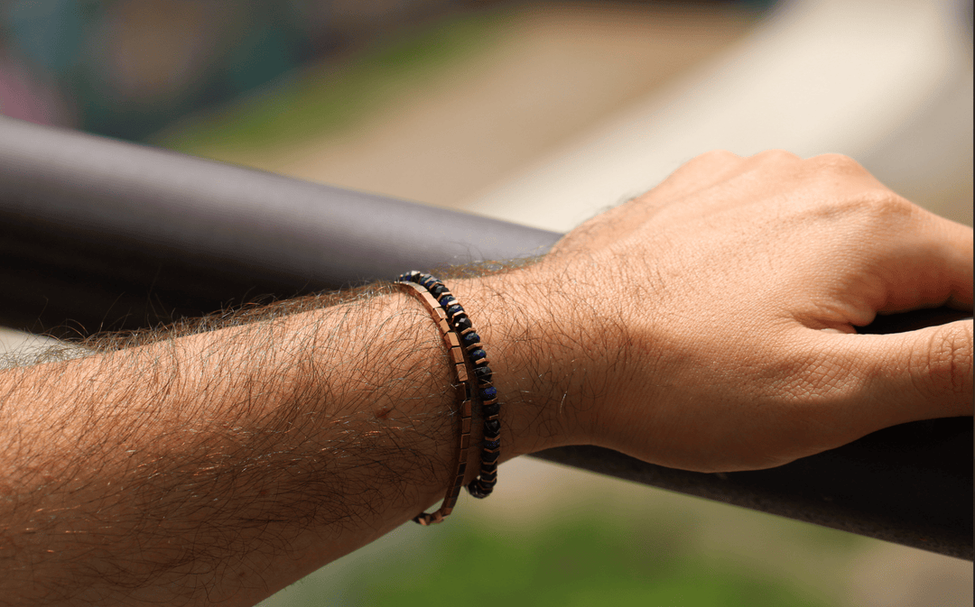 Titanium Hematite Rectangle bracelet stacked with dark beads on a wrist by an outdoor railing