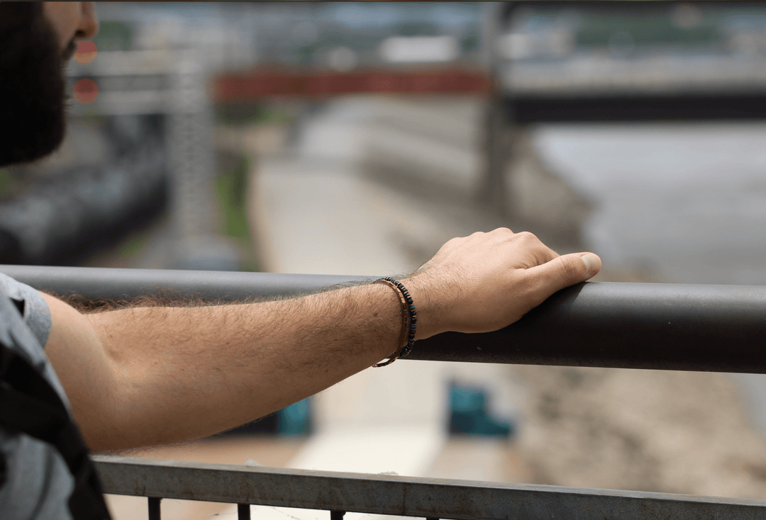 Titanium Hematite Rectangle bracelet on an outstretched wrist beside an outdoor railing