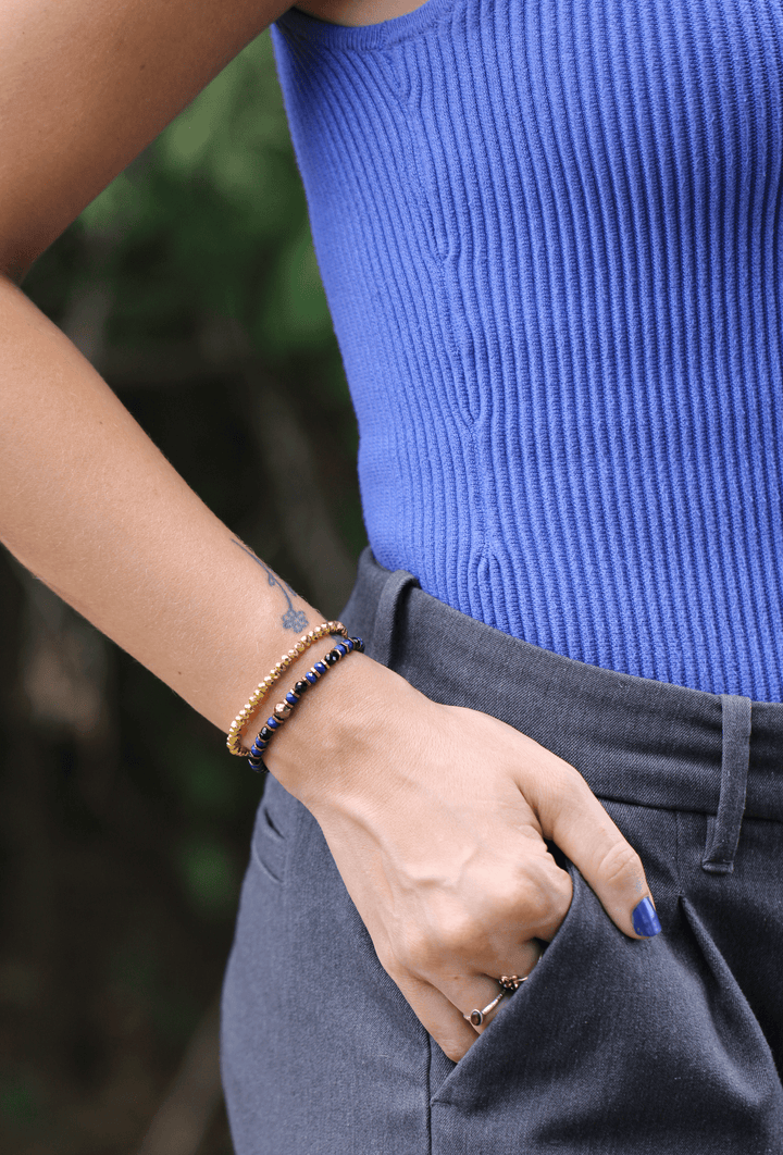 Titanium Hematite Rondelle bracelet stacked with purple beads beside a blue top