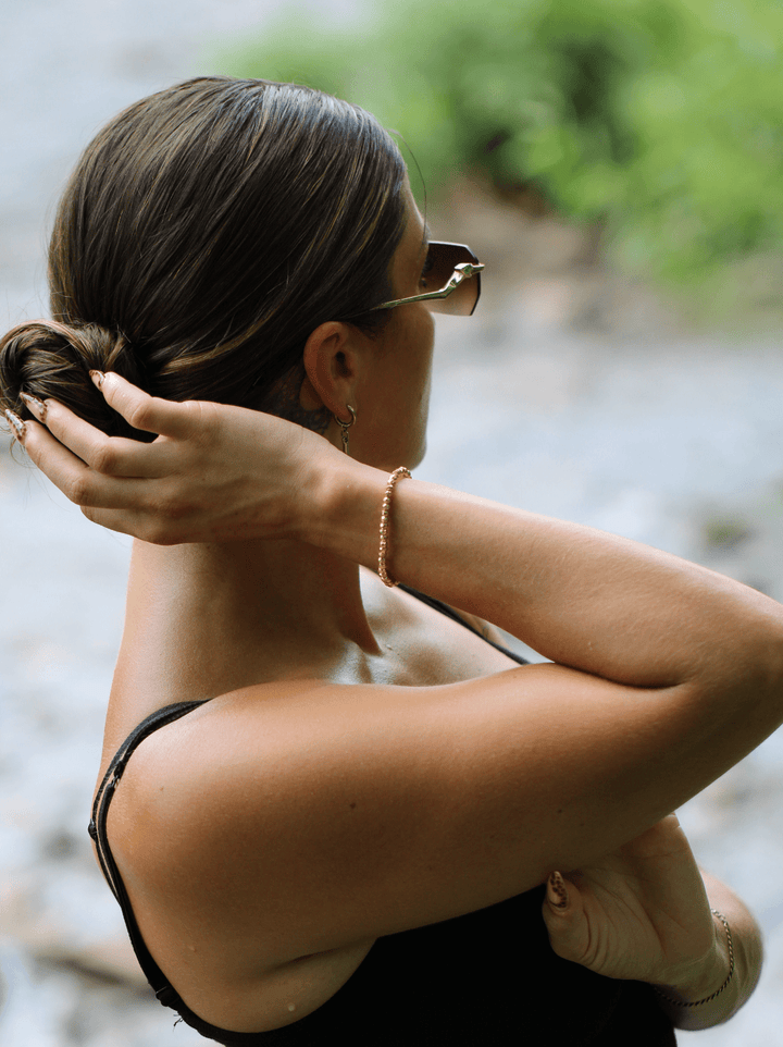 Titanium Hematite Rondelle bracelet on a raised wrist as a woman adjusts her hair outdoors