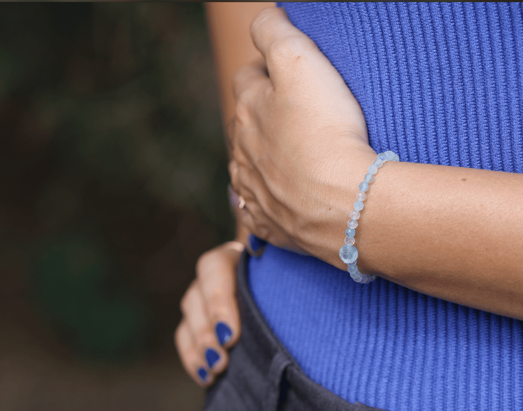 True Compassion aquamarine flower bracelet on a wrist held across a blue top