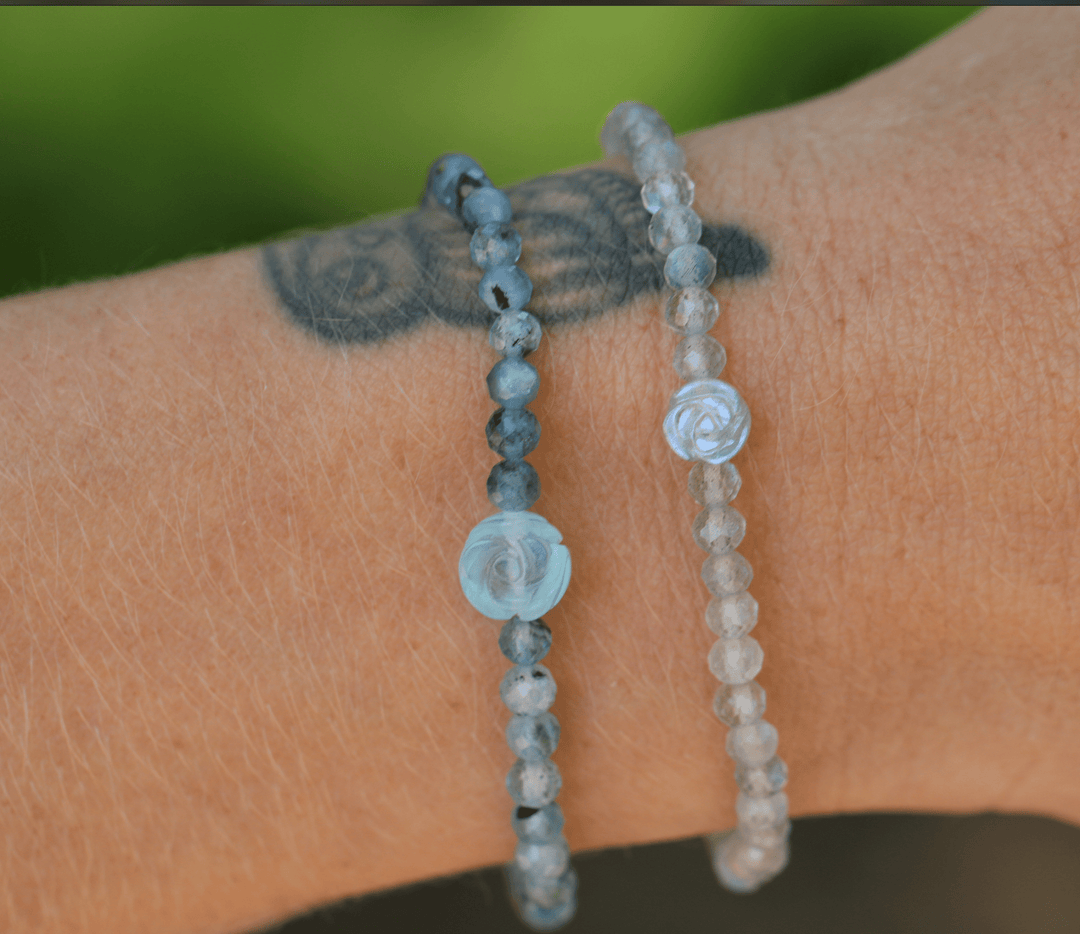 True Compassion aquamarine bracelet beside a pale beaded bracelet on a tattooed wrist